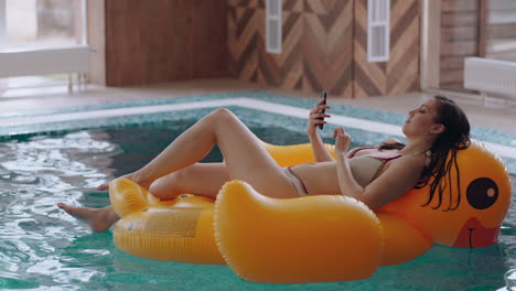 woman-is-relaxing-in-pool-in-hotel-lady-is-lying-on-yellow-inflatable-duck-and-viewing-news-in-social-media